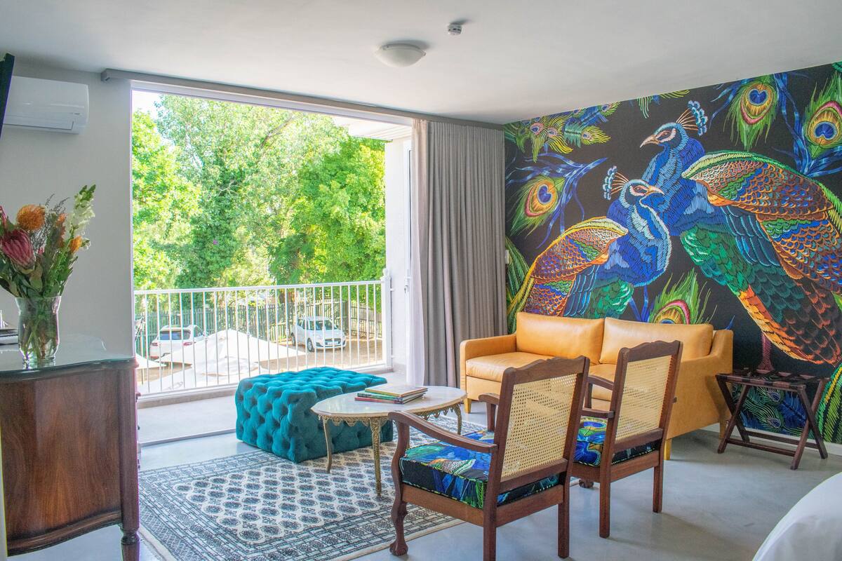 Una habitación con un mural de pavo real, un sofá, una silla, una pequeña mesa y vistas al exterior con vegetación.