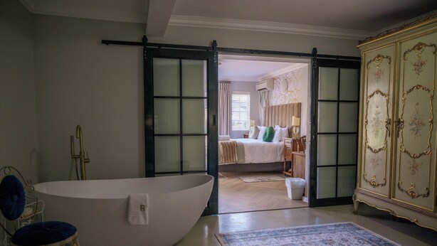 Een ruime badkamer met een vrijstaand bad, een grote spiegel en een decoratieve stoel.