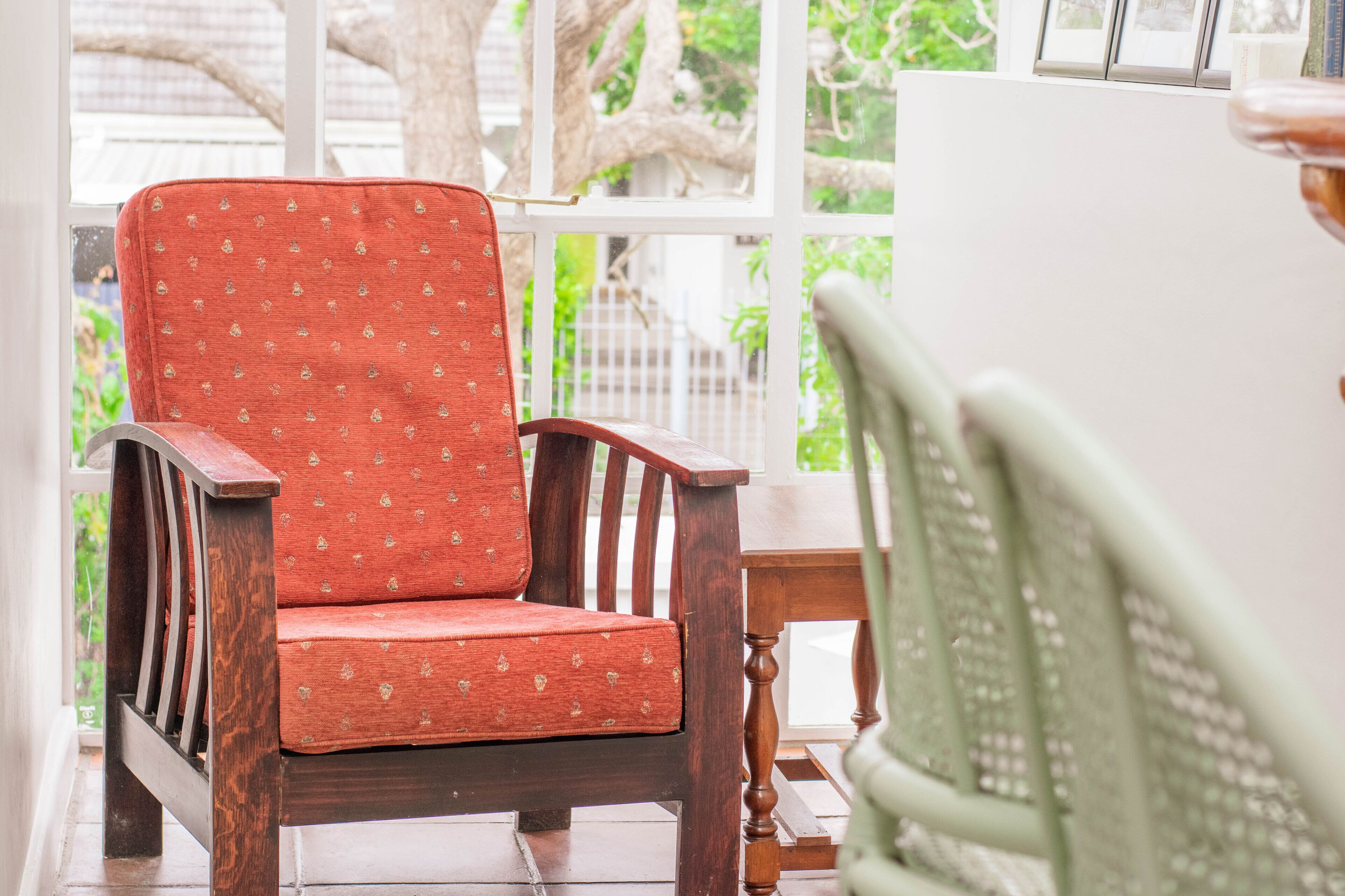 A wooden chair with a red cushion and a green chair with a patterned backrest.