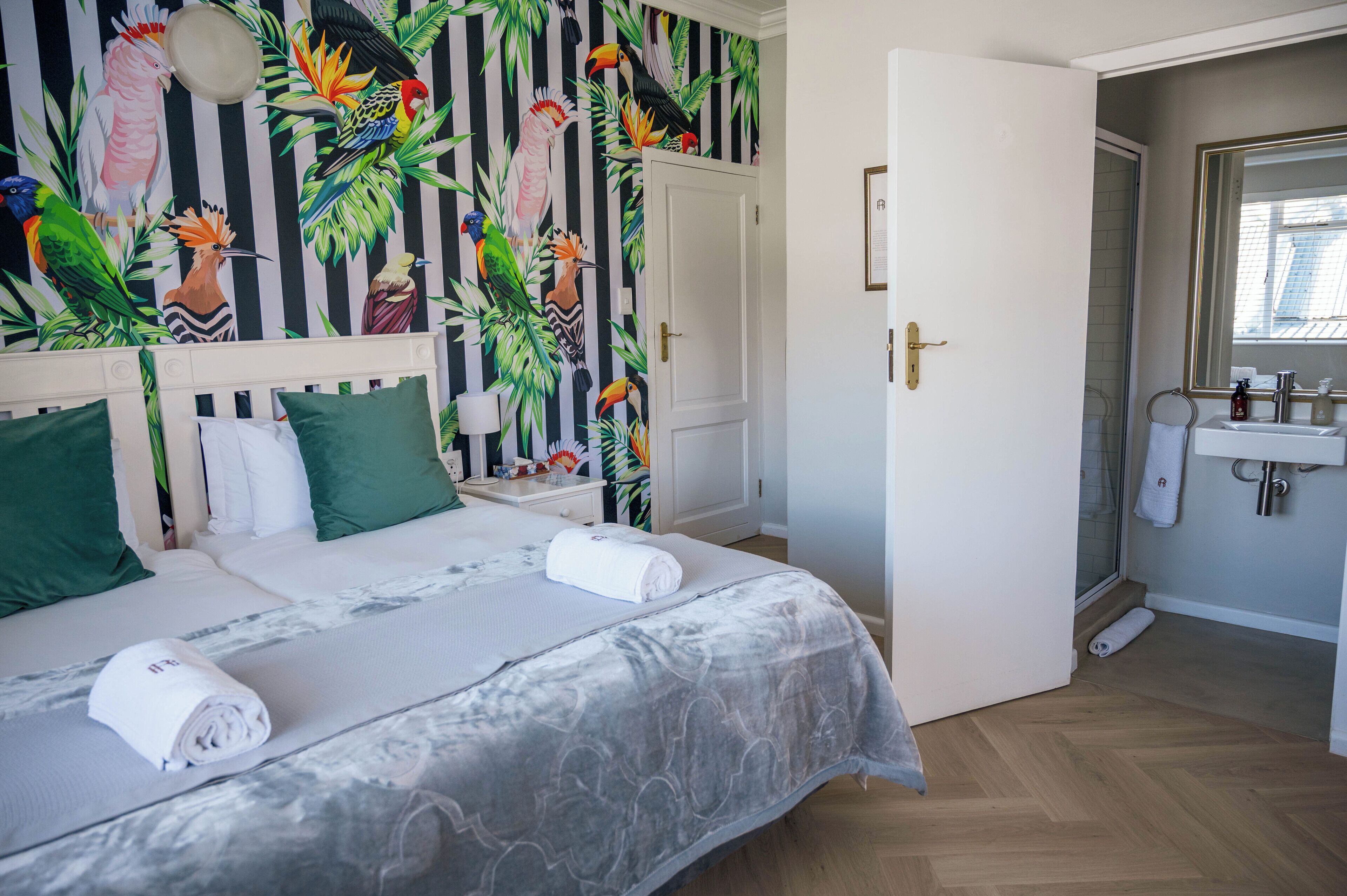 A hotel room with a bed, a nightstand, a bathroom with a sink and mirror, and a door leading to another room.