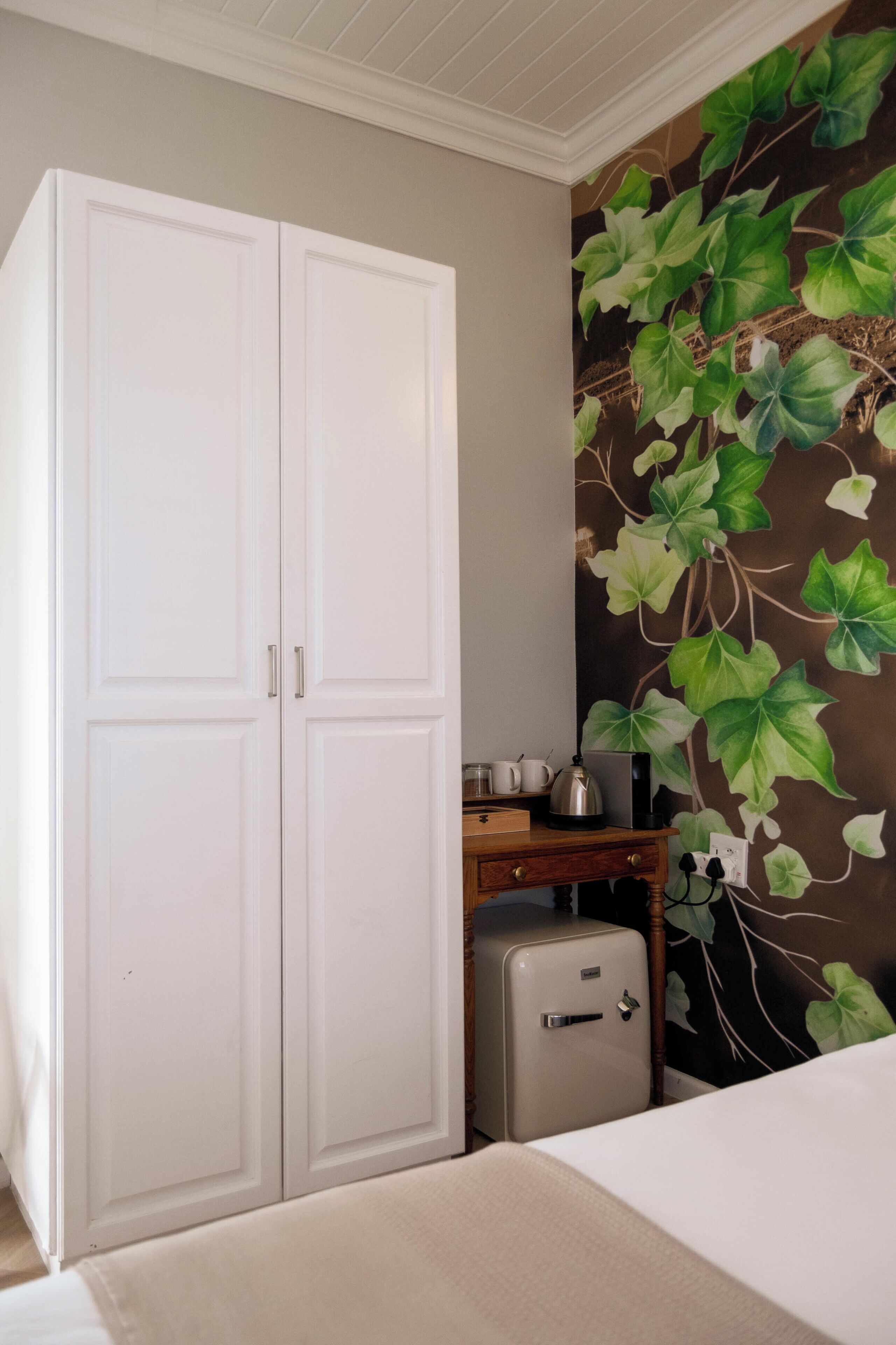 A room with a wardrobe, a small desk with a kettle, and a vintage-style refrigerator.