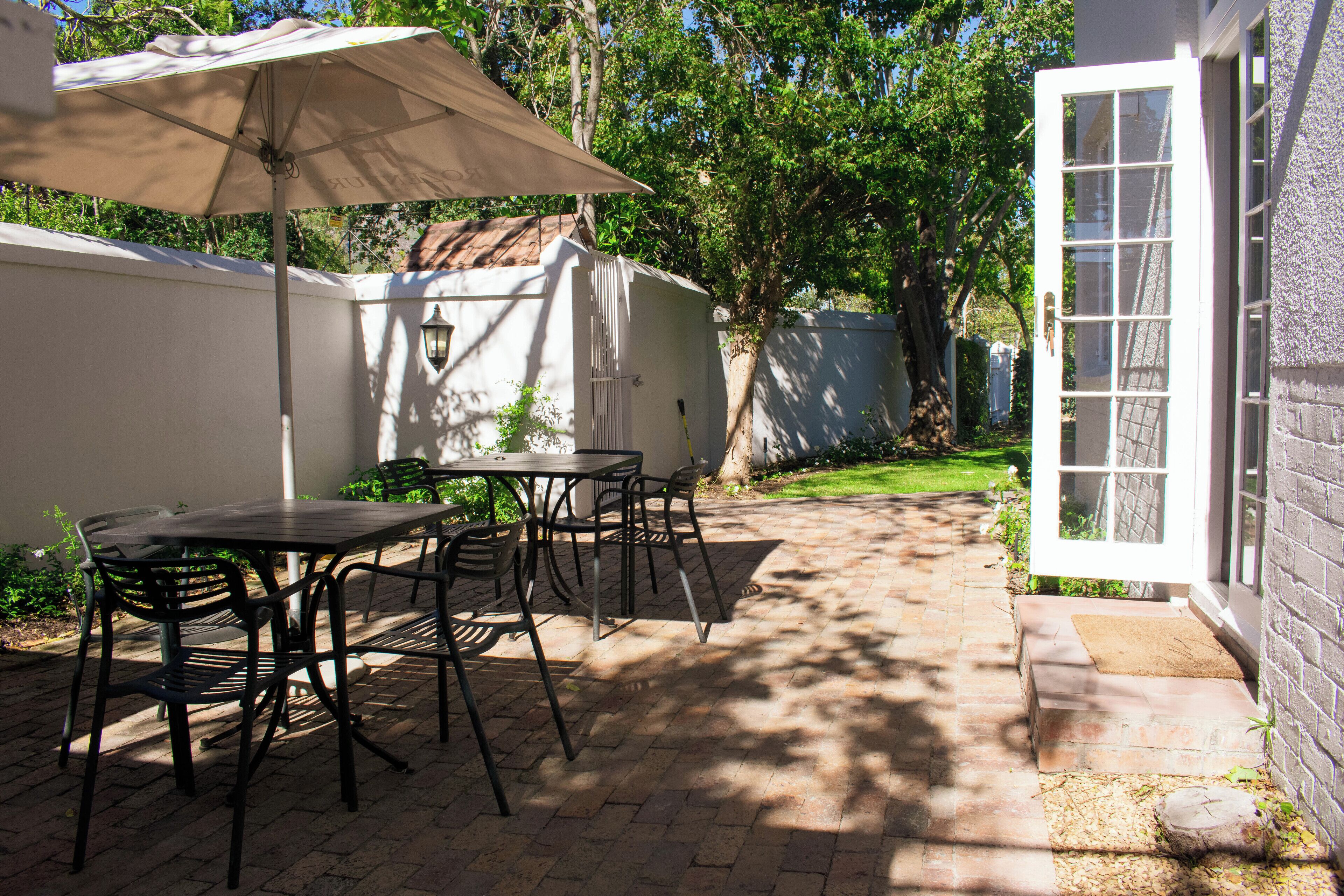 An outdoor patio with a table and chairs, a large umbrella, and a white door.