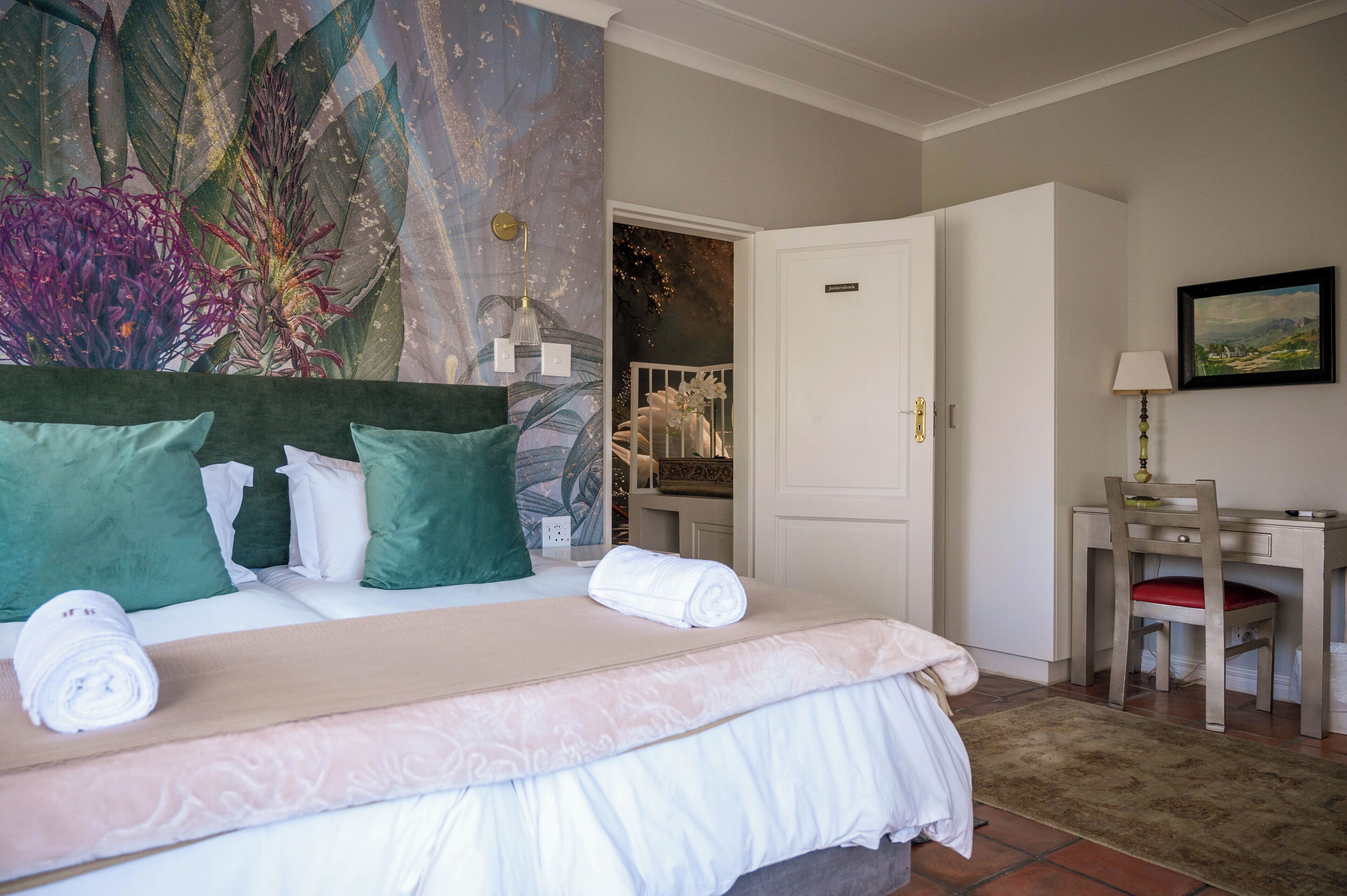 Une chambre avec un grand lit, des oreillers verts et blancs, un bureau avec une chaise et un tableau accroché au mur.