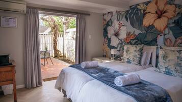 A hotel room with two beds, a large floral mural on the wall, and a view of the outside garden.