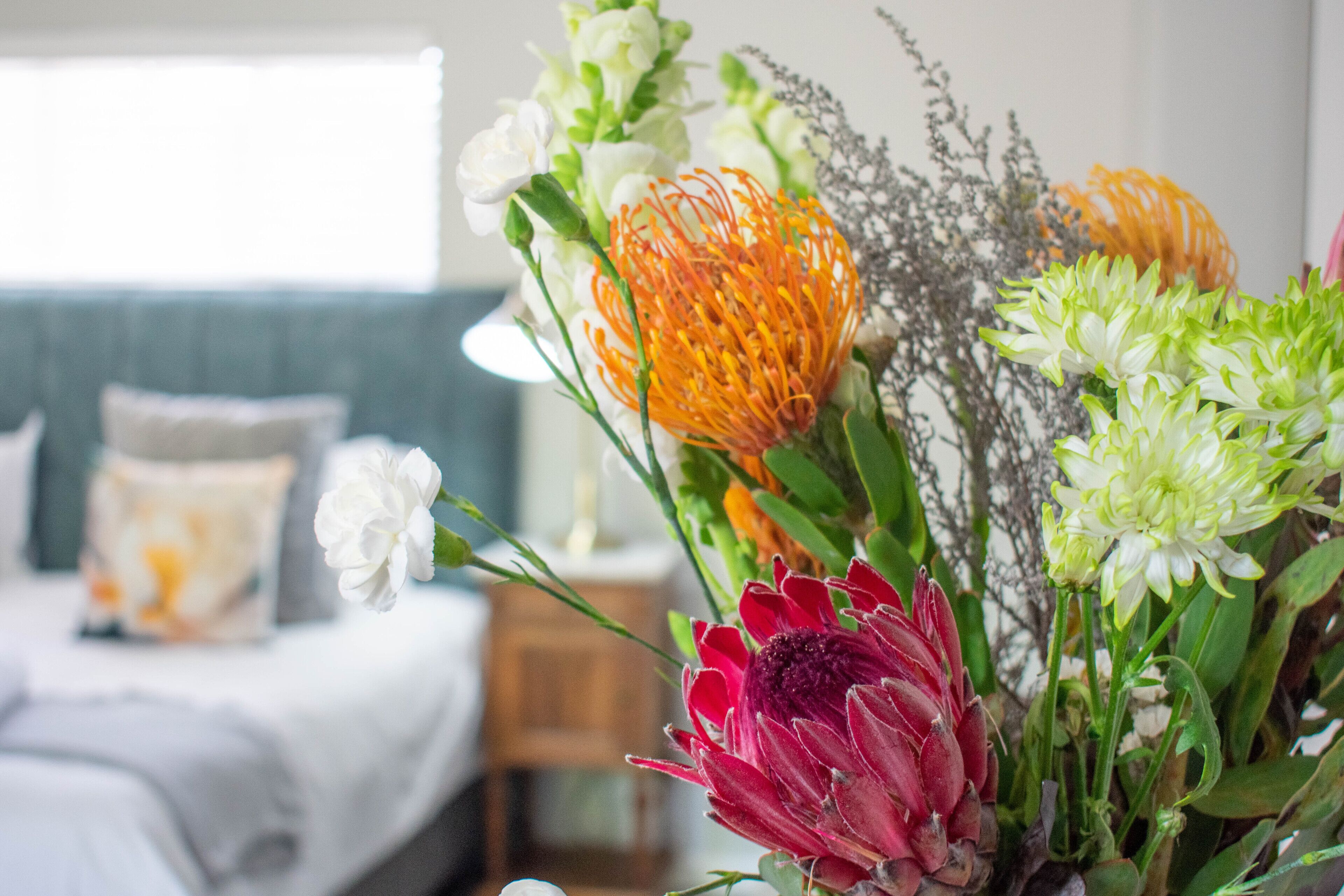 A room with a bed, a bedside table, and a vase of flowers.