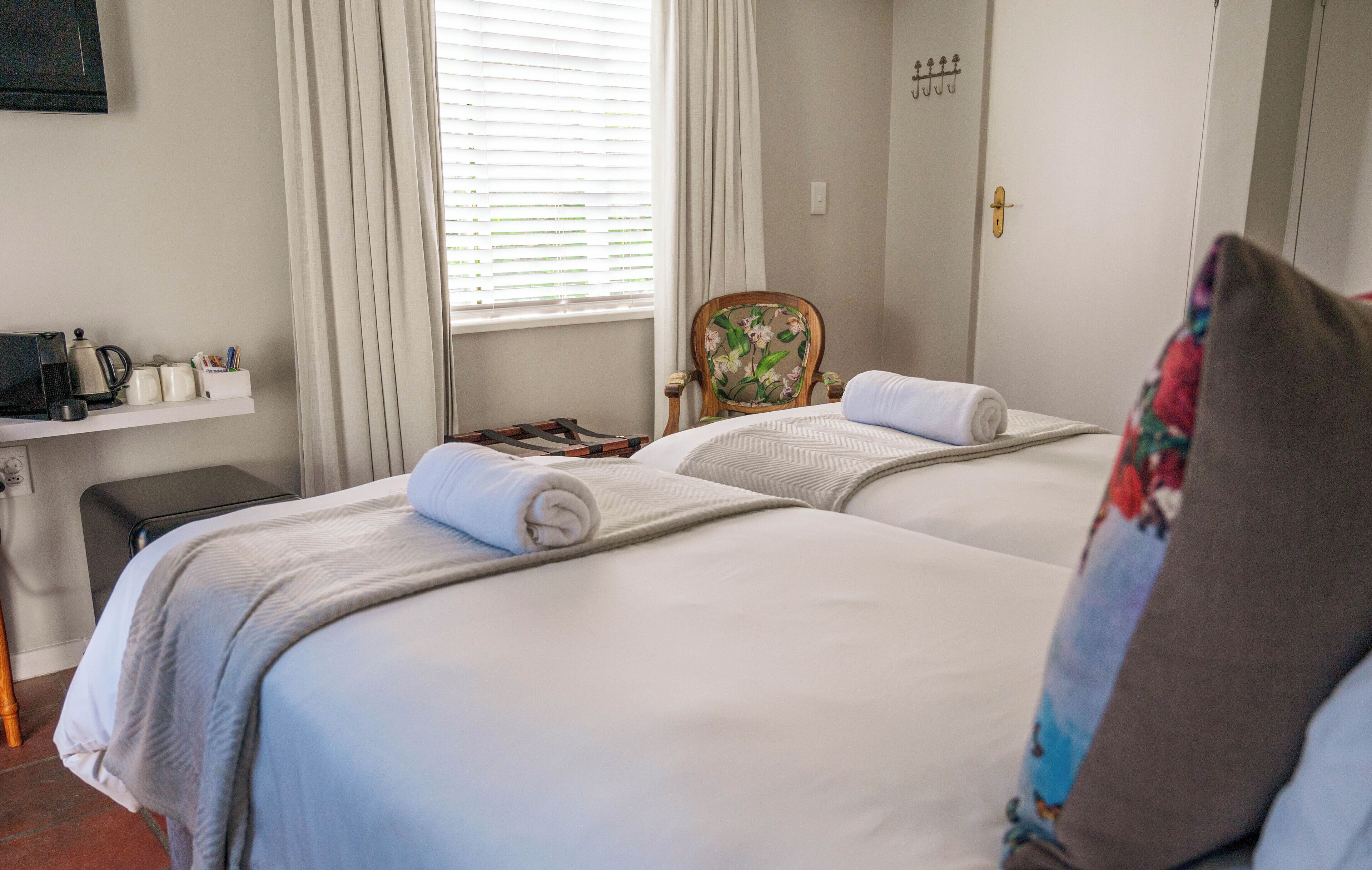 Une chambre d’hôtel avec deux lits, une chaise, une petite table avec une bouilloire et une fenêtre avec des rideaux.