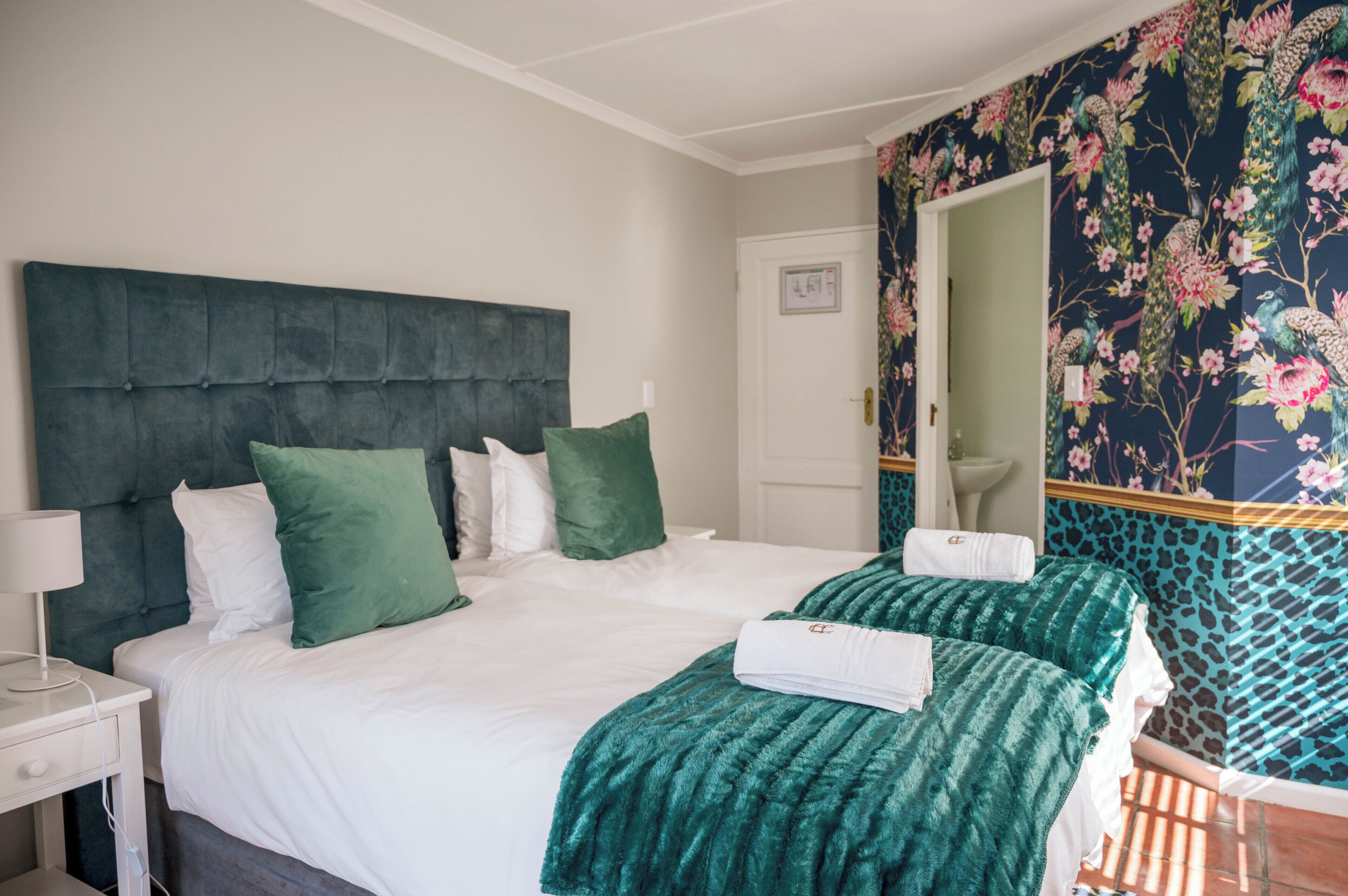 Quarto de hotel com uma cama grande, duas almofadas, mesa de cabeceira com abajur e um espelho.