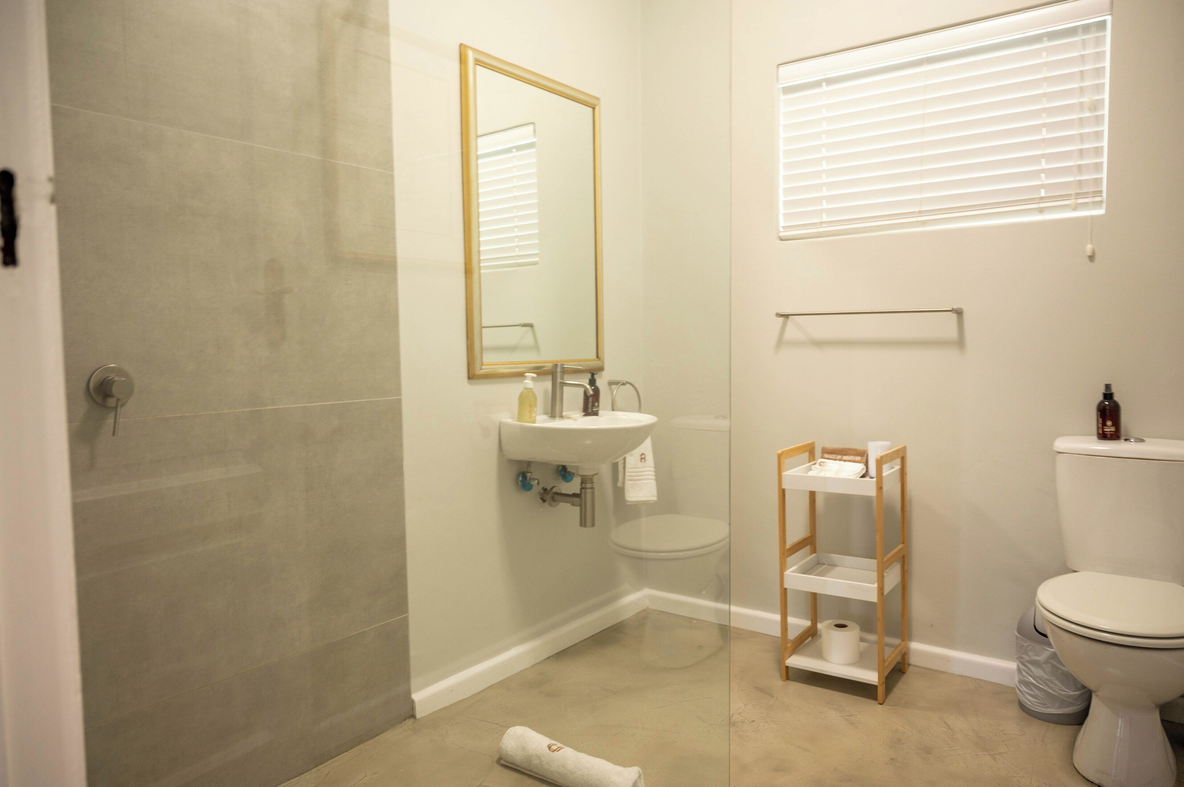 Un baño con ducha, lavabo, inodoro y un pequeño estante de madera.
