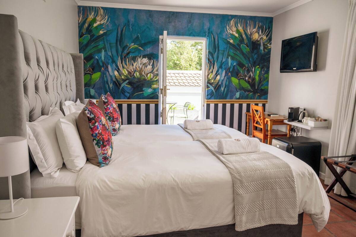 Una habitación de hotel con una cama grande, televisión, escritorio con silla y un mural en la pared.
