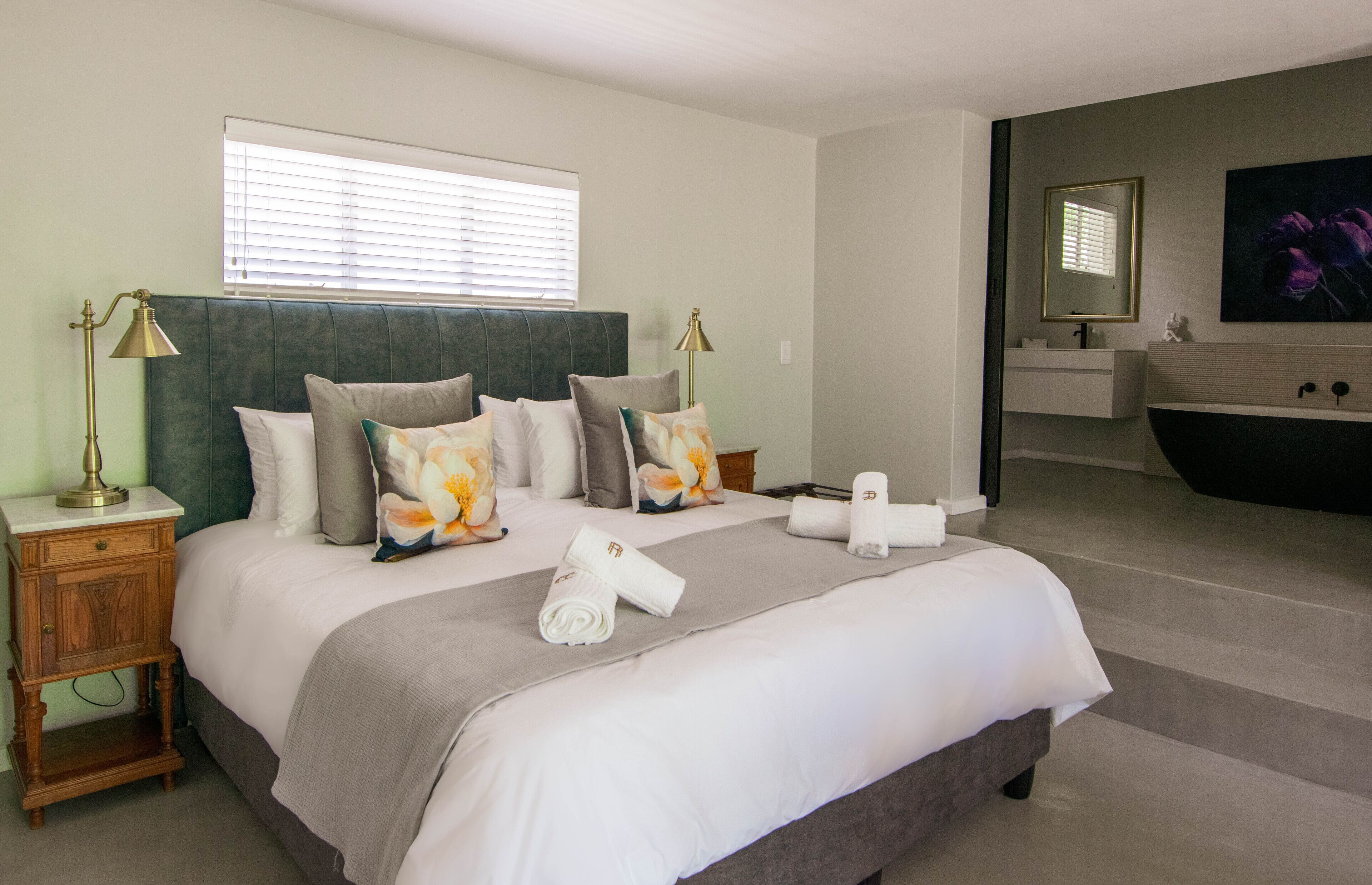 A hotel room with a large bed, bedside lamps, a vanity with a mirror, and a bathtub.