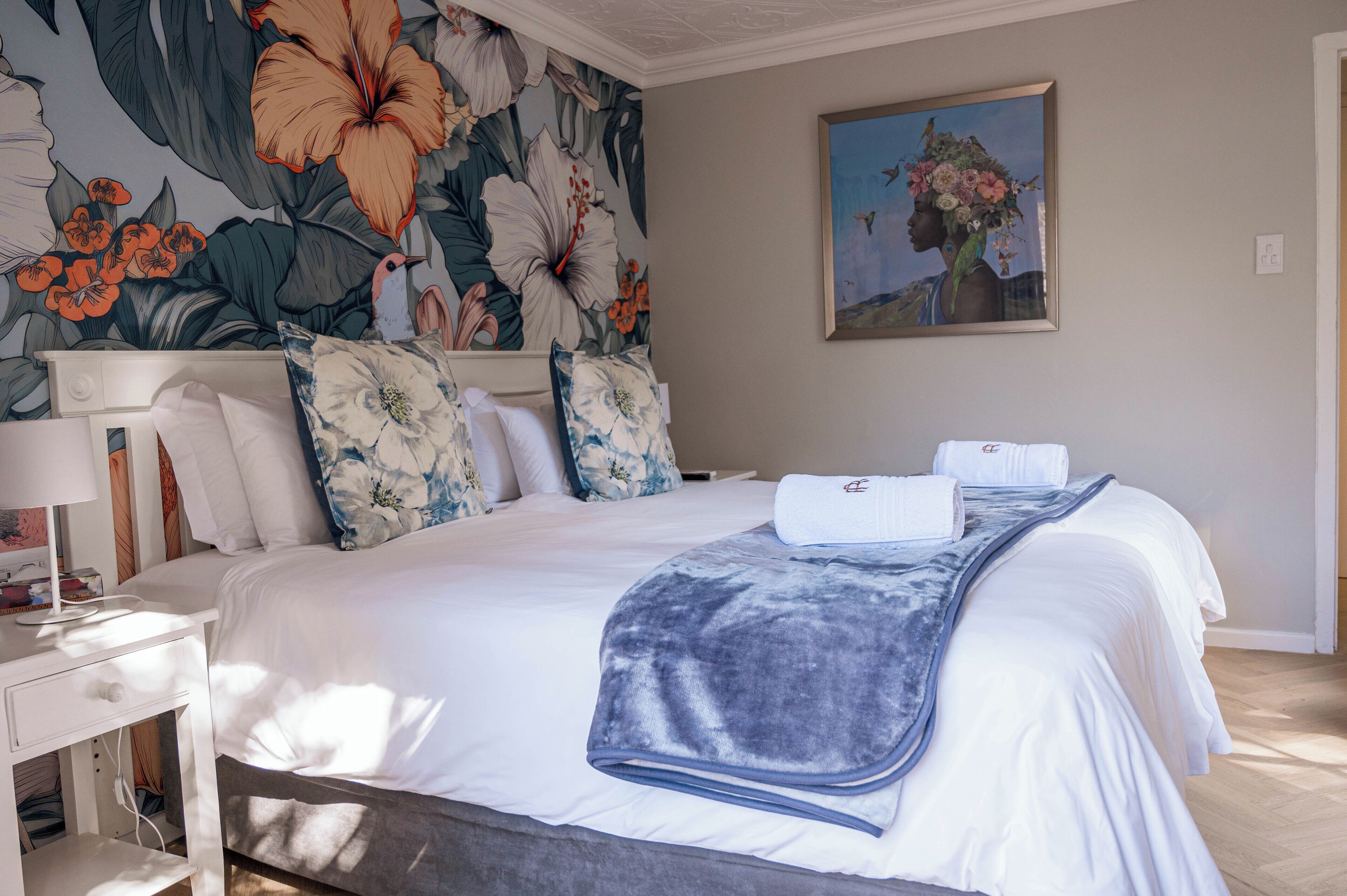 A neatly made bed with a blue blanket, white pillows, and a floral-patterned headboard.