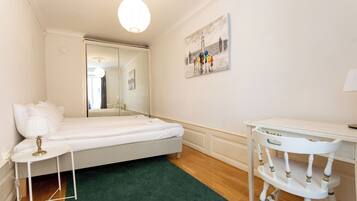 A bedroom with a bed, a desk, a chair, a green rug, and a painting on the wall.