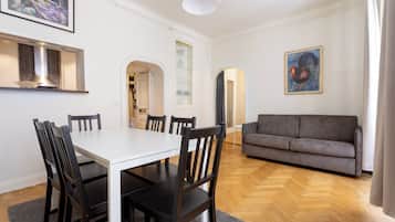 Un comedor con una mesa blanca y sillas oscuras, un sofá gris y piso de madera.