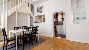A dining area with a white table and chairs, a staircase, and a kitchen visible through an archway. - ApartDirect Gamla Stan III (Stockholm)