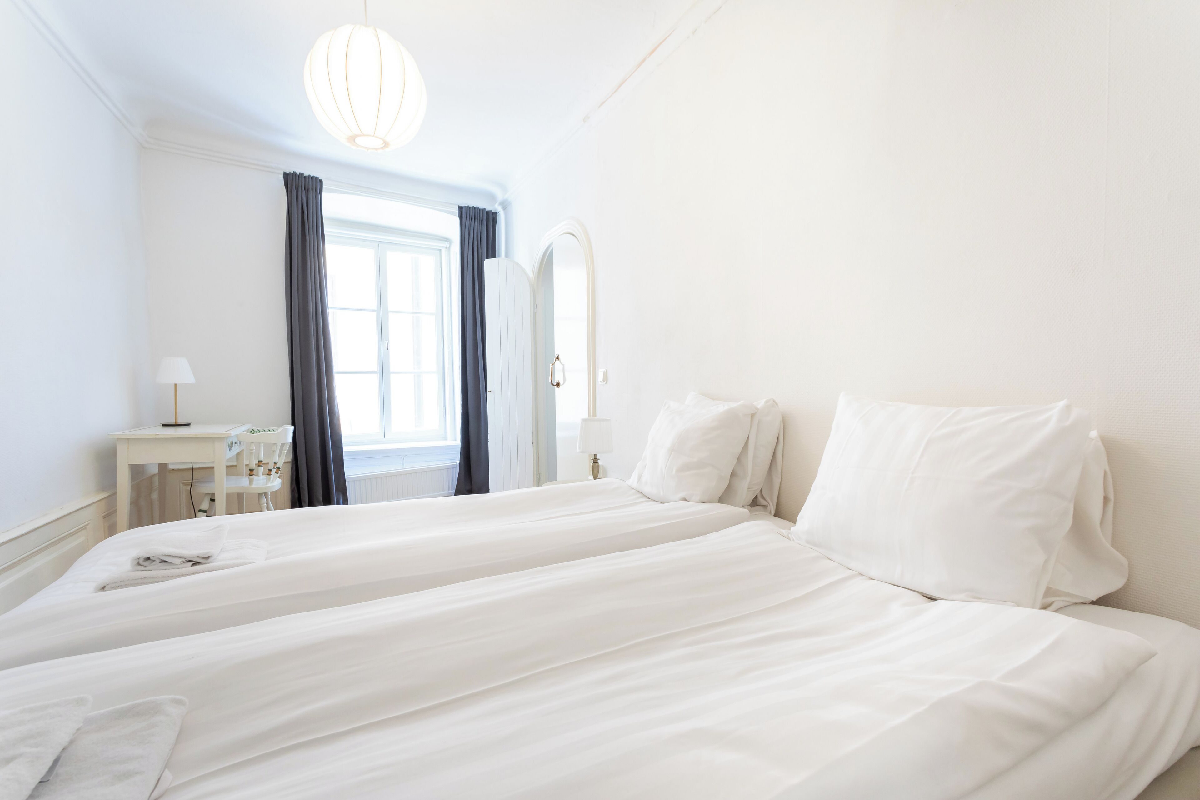 A hotel room with two beds, a desk with a lamp, and a window with curtains.