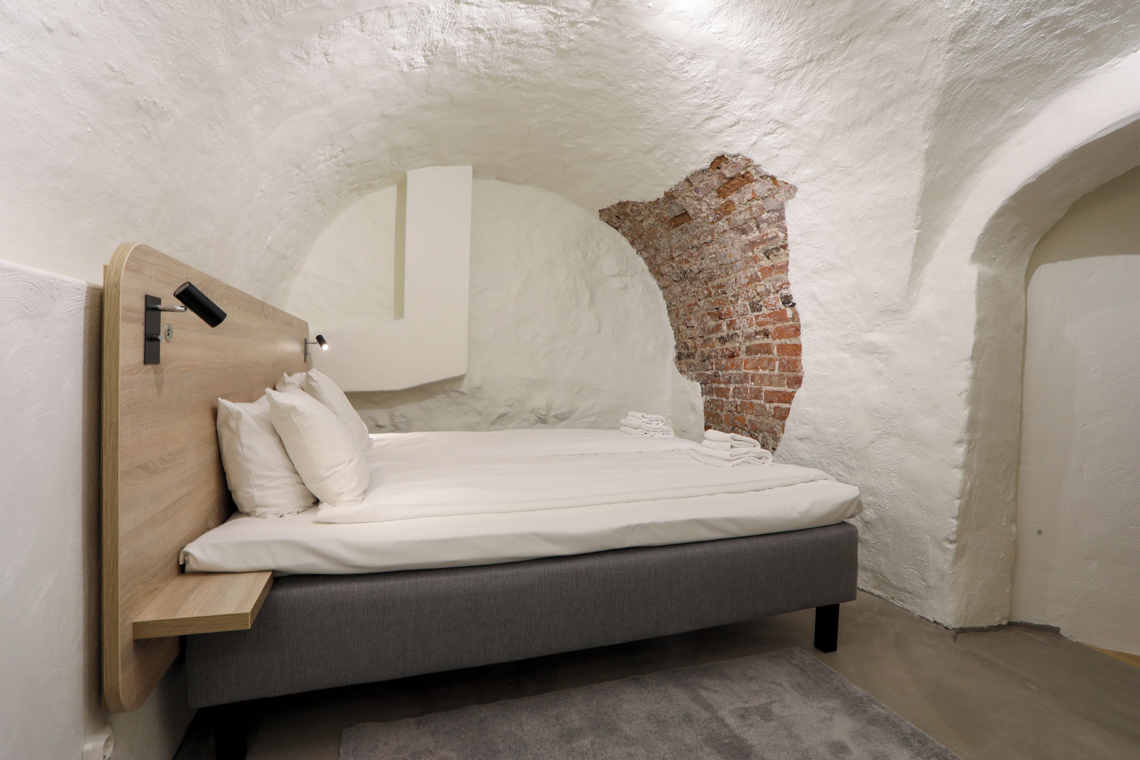 Ein Schlafzimmer mit einem Bett, einem Holzkopfteil, einer Ziegelwand und einer weißen Decke.