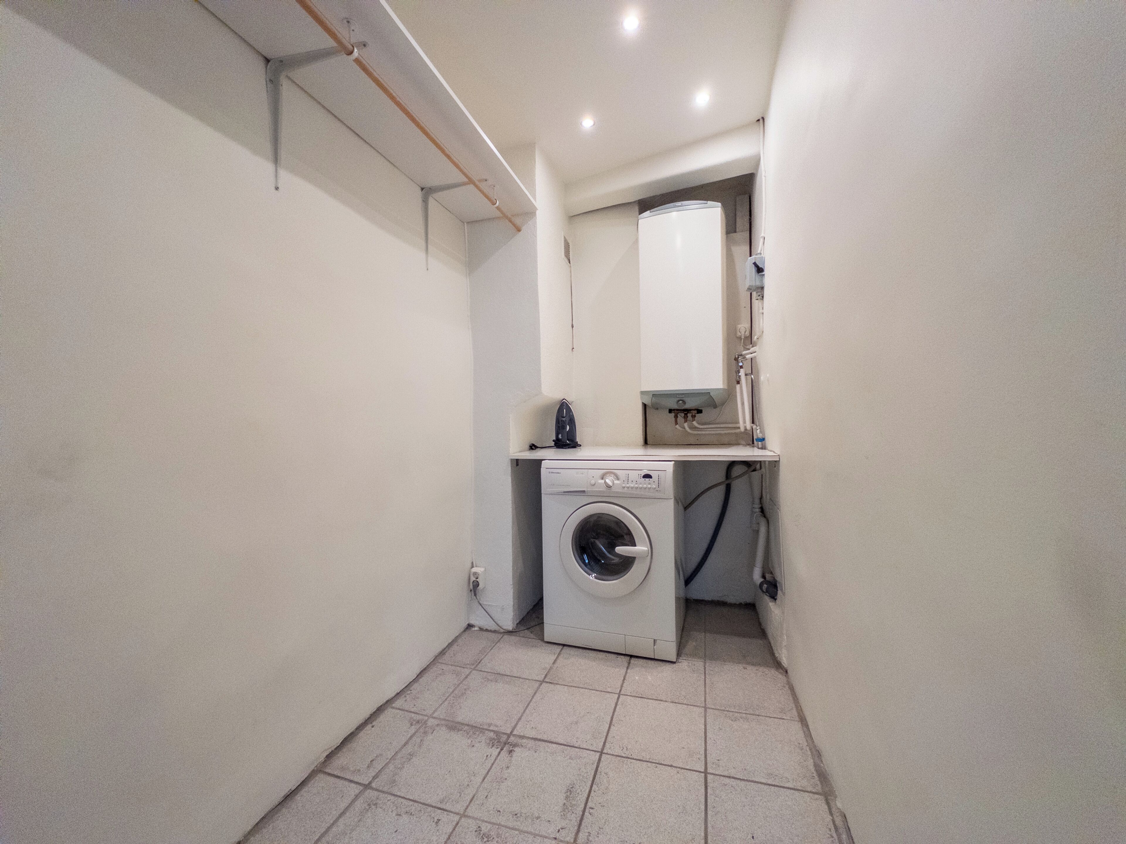 A compact laundry room with a washing machine, a small countertop, and a mirror.