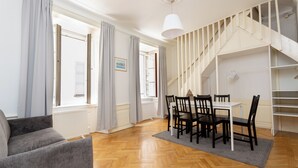 A spacious living room with a wooden herringbone floor, a dining table with chairs, a grey sofa, and a staircase with a white railing. - ApartDirect Gamla Stan III (Stockholm)