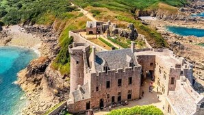 Un castillo de piedra histórico con un patio central, rodeado de terreno rocoso y vistas al mar.