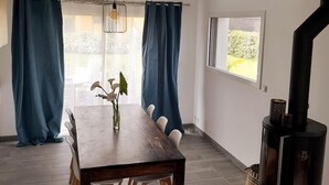 Un comedor con una mesa de madera, cortinas azules, una lámpara colgante y una estufa de leña.