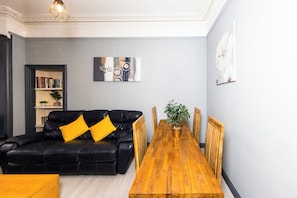 Een moderne woonkamer met een zwarte leren bank, een houten eettafel en een boekenkast.