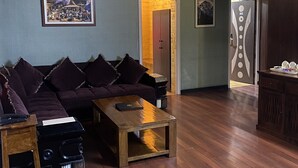 Ein modernes Wohnzimmer mit einem dunkelgrauen Sofa, einem Couchtisch aus Holz und einem Deckenventilator. An der Wand hängt ein gerahmtes Bild und eine Tür mit ungewöhnlichem Design.