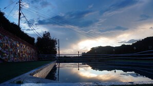Eine friedliche Außenansicht mit einem spiegelnden Wasserspiegel, einer Ziegelwand mit farbenfrohen Mustern und einem klaren Himmel mit Wolken.