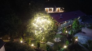 Luchtbeeld van een hotel met een goed verlicht buitengebied, inclusief een ronde tuin met zitplaatsen en een trap naar een hoger gelegen niveau.
