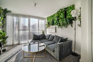 A modern living room with a sectional sofa, a glass coffee table, and a large window with blinds. - Leicester - Apartment - Sleeps 2 - 97ws (Leicester)