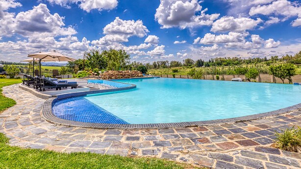 A swimming pool with a stone deck, lounge chairs, and a pergola. - Villa Tasha Luxury suites (Lanseria)
