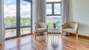 A room with two beige armchairs, a small round table with a potted plant, and large windows with curtains. - Villa Tasha Luxury suites (Lanseria)