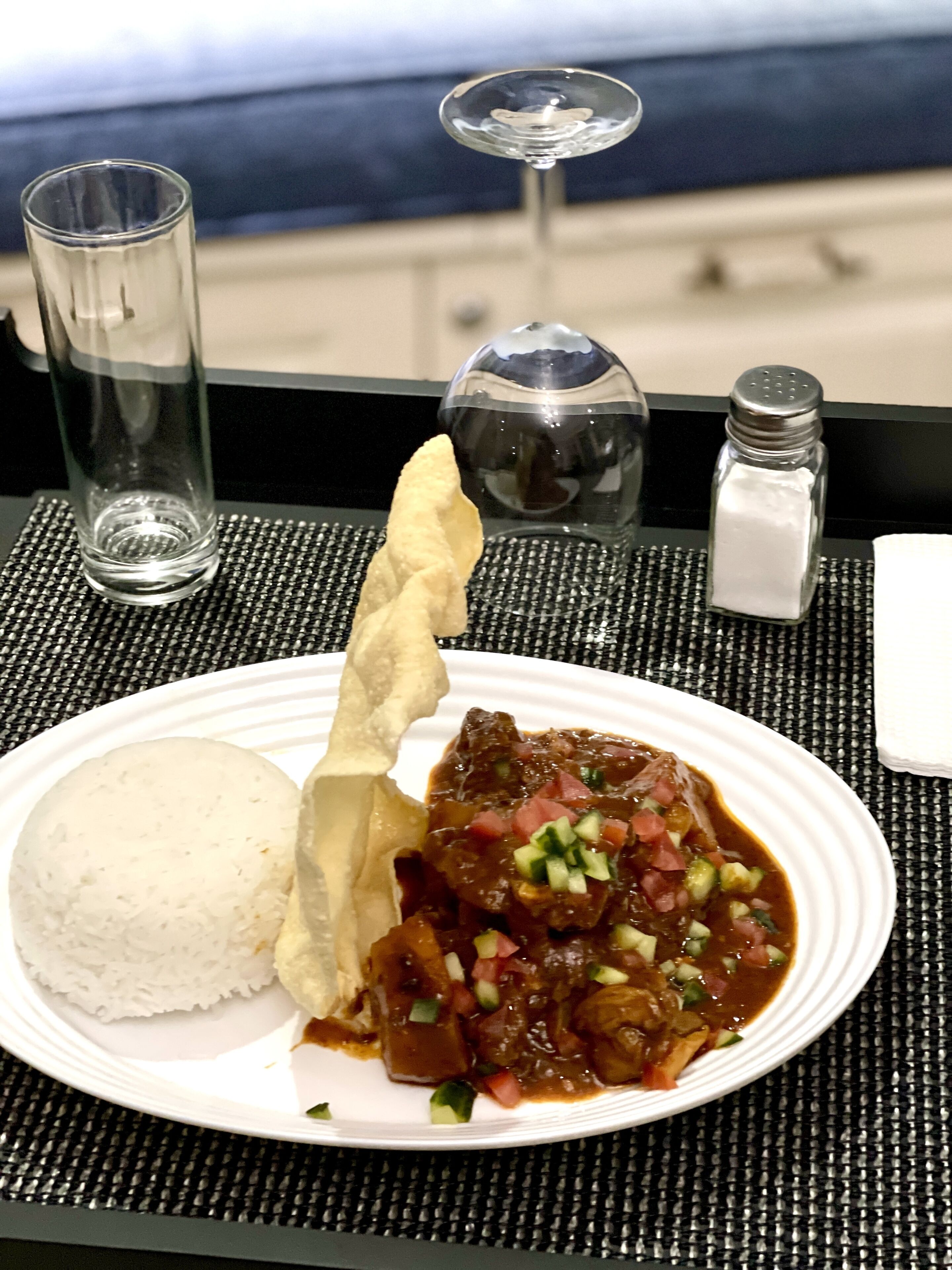 A plate with rice, a breadstick, and a meat dish, accompanied by a glass of water and salt and pepper shakers on a table.