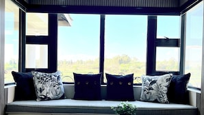 A cozy seating area with a built-in bench, two windows, and a small table with a plant and magazines. - Villa Tasha Luxury suites (Lanseria)