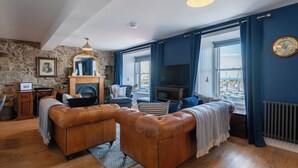 Een woonkamer met een stenen muur, een open haard, een televisie en uitzicht op de haven.