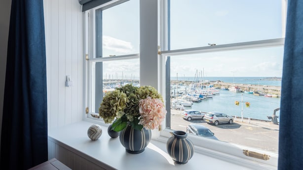 Uitzicht op een baai vanuit een raam, met een bloevas op de vensterbank.