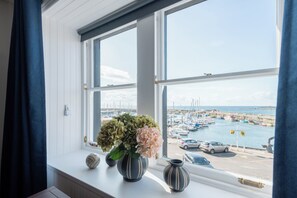 Näköala lahdelle ikkunasta, jonka ikkunalaudalla on maljakko täynnä kukkia.