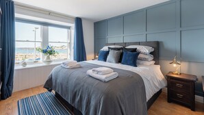 Een slaapkamer met een groot bed, een nachtkastje, een raam met gordijnen en uitzicht op zee.