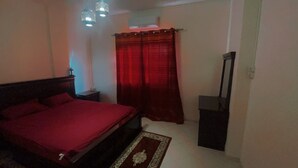 A bedroom with a bed, a nightstand, a mirror, a red curtain, and a ceiling fan. - Appartement Équipé et Climatisé (Marrakech)