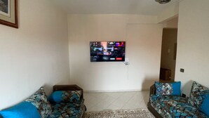 A living room with two patterned sofas, a flat-screen TV mounted on the wall, and a patterned rug on the floor. - Appartement Équipé et Climatisé (Marrakech)