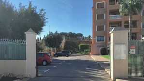 Een afgesloten parkeergebied met een rode auto en een zwarte auto, voor een gebouw met meerdere verdiepingen en balkons.