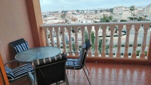 Een balkon met een ronde tafel en vier stoelen, een uitzicht op een stadsbeeld en een betegelde vloer.