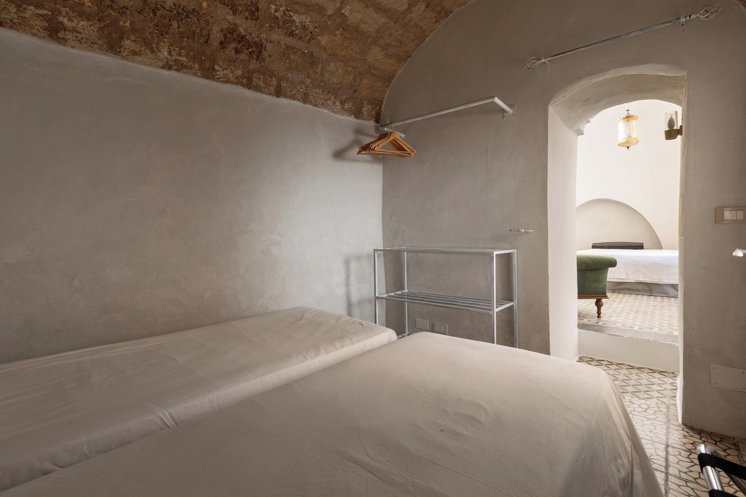 Quarto minimalista com uma cama de solteiro, uma estante de metal e um candeeiro suspenso.