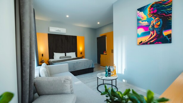 Une chambre d’hôtel moderne avec un lit, un canapé, une petite table ronde et un tableau au mur.