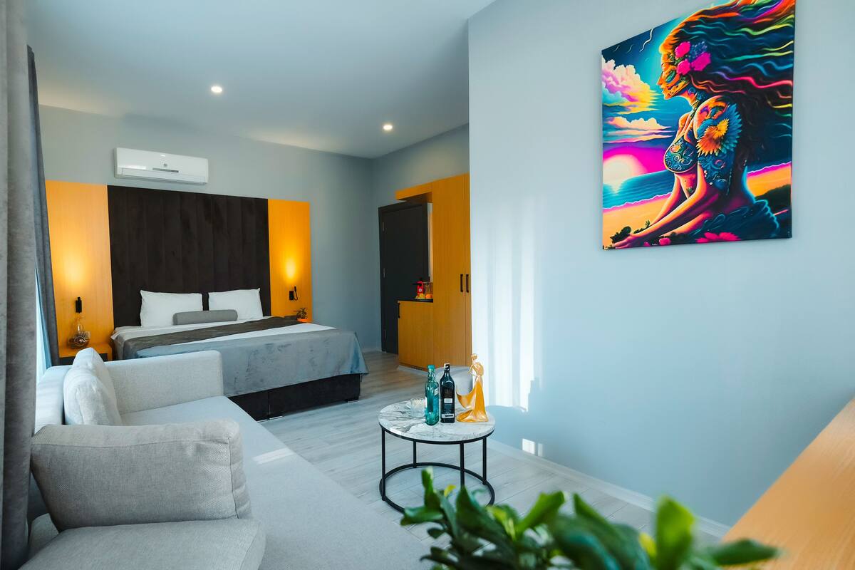 A modern hotel room with a bed, a sofa, a small round table, and a painting on the wall.