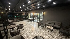 Un espace aménagé, à la fois intérieur et extérieur, avec un sol à motifs, des tables, des chaises et un canapé.