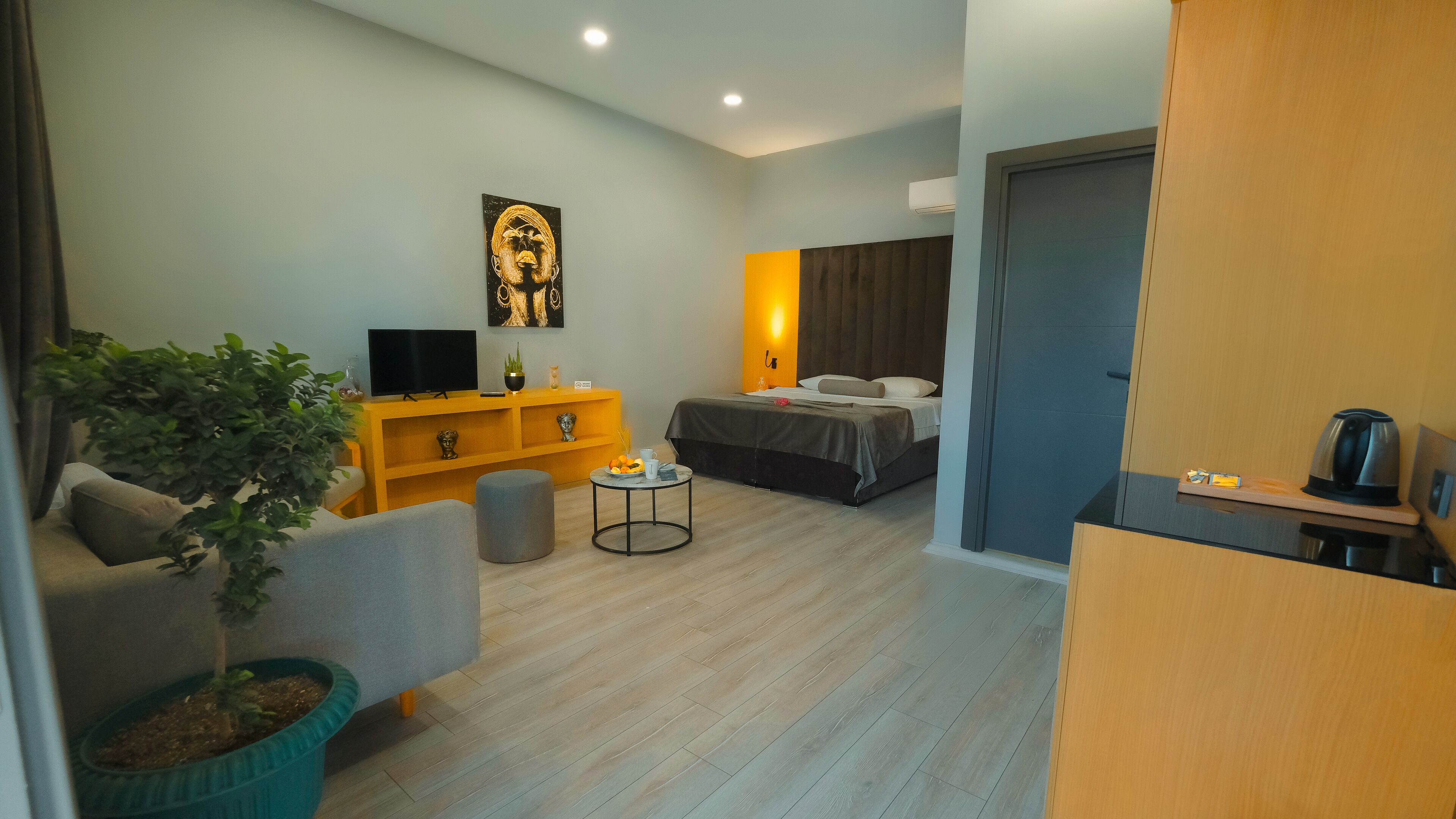 Una habitación de hotel moderna con un sofá, una mesita con fruta, un televisor, una cama y un baño visible a través de una puerta abierta.