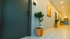 Un couloir avec un arbre en pot, une porte et un panneau fixé au mur.