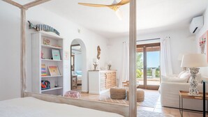 Une chambre avec un grand lit, une armoire blanche, un miroir et une vue sur le balcon.