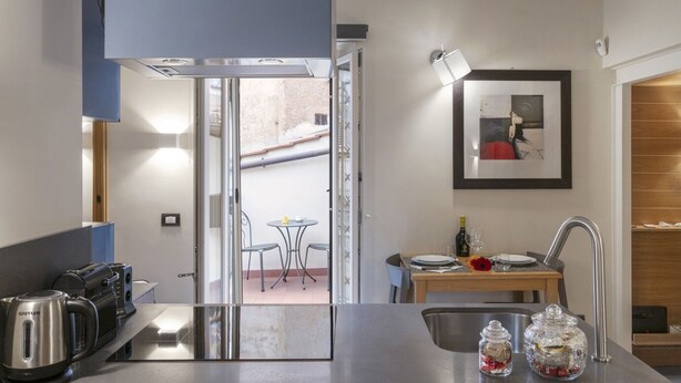 A modern kitchen with a built-in stove, a sink, and a dining area with a table and chairs. - Flat Piazza del Popolo central (Roma)
