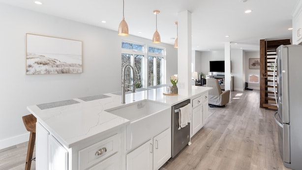 Une cuisine moderne dotée d’un grand îlot central, de luminaires suspendus et offrant une vue sur l’extérieur.